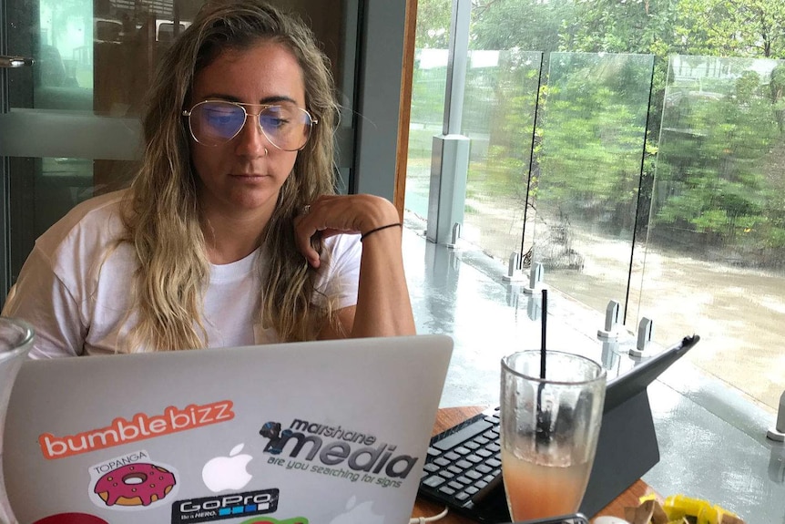 Tara Leach stares at her computer surrounded by water and a juice at a cafe