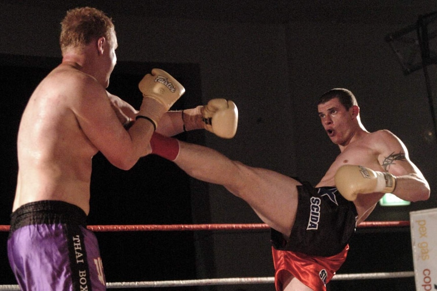 Two men on a boxing ring fighting, with one kicking another in a long extended kick.