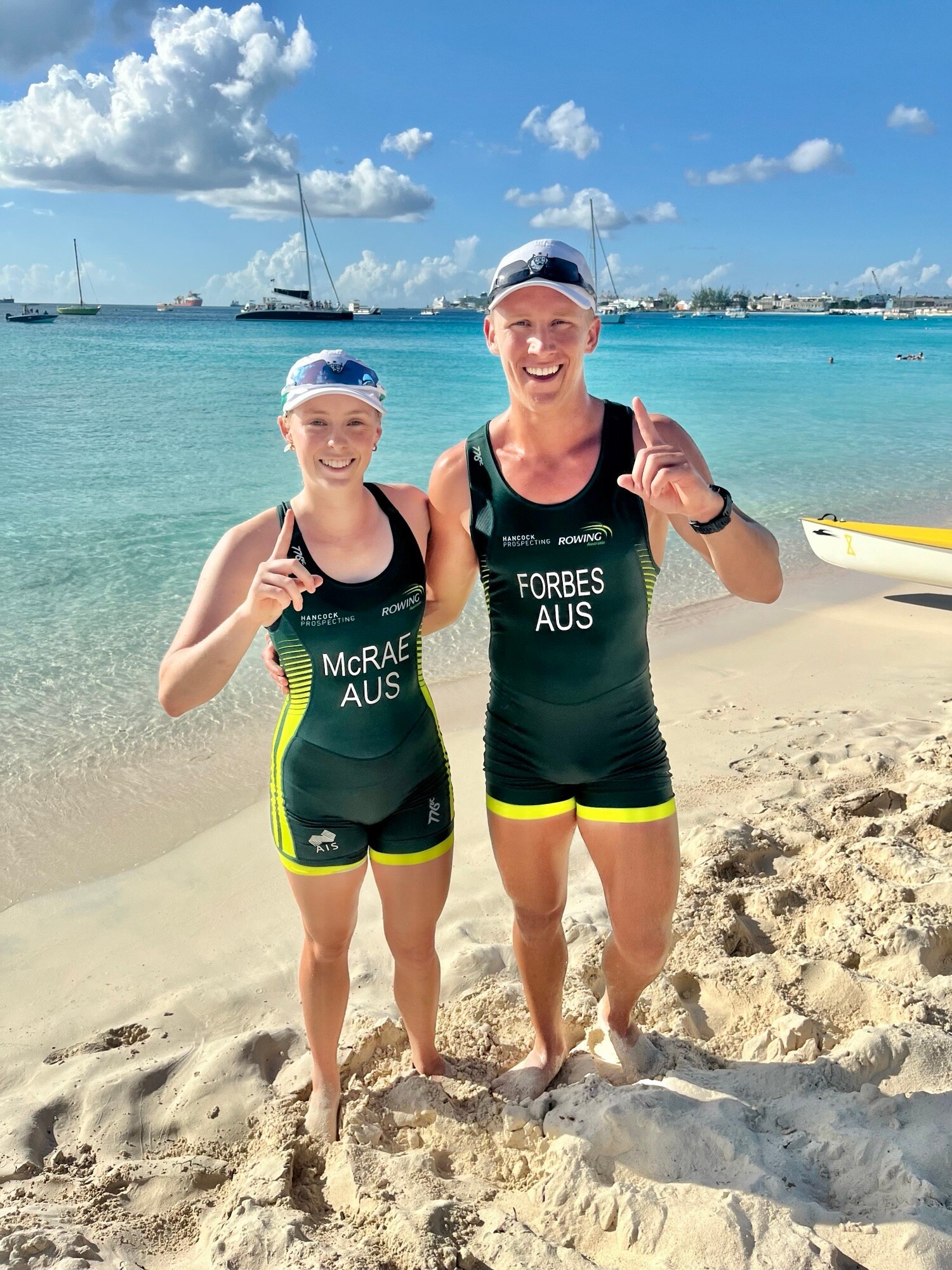 Un hombre y una mujer están juntos en la playa y sonríen al equipo de natación australiano. 