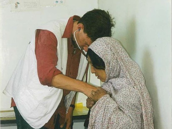 Brett Sutton puts a stethoscope to the chest of a woman wearing a headscarf