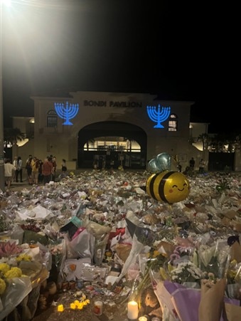 Uma abelha inflável em um mar de buquês de flores e duas velas acesas.