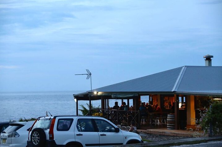A wide shot of a beachfront bar filled with people on Christmas Island with the ocean and cars nearby.