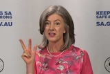 A woman wearing a pink top shows two fingers