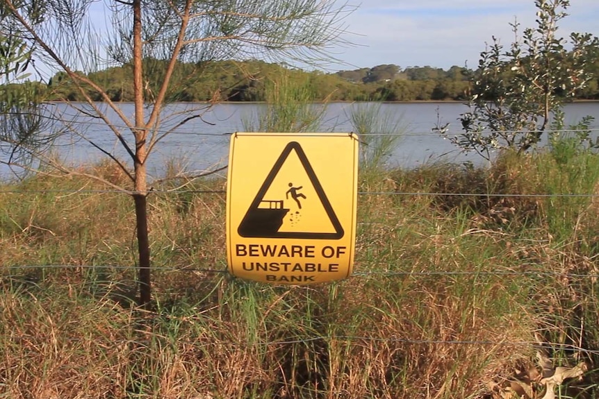 A sign in front of a river which says 'Beware of Unstable Bank'