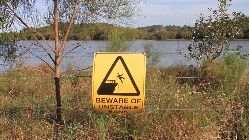 A sign in front of a river which says 'Beware of Unstable Bank'