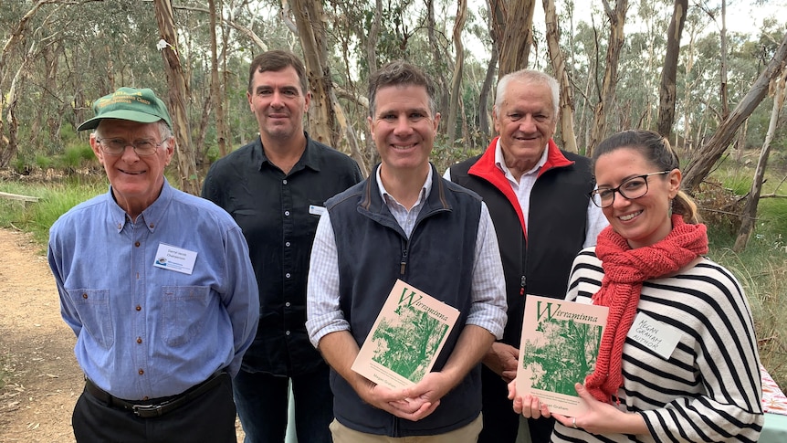 Group of people stand in bushland, some holding books, for Wirraminna book launch