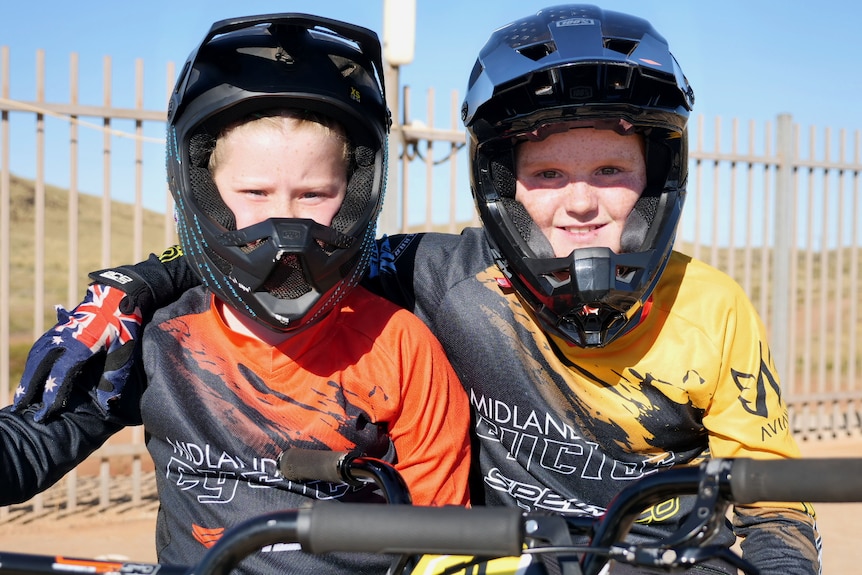Two children in cycling gear with helmets have their arms around each other