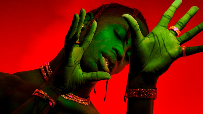Press shot of rapper Travis Scott; red background; subject with green light