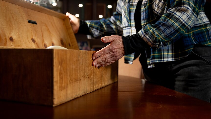 A woman opens a small wooden box on a table.