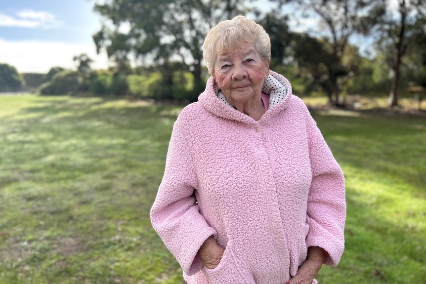 An elderly lady in a pink jumper stands in a green paddock