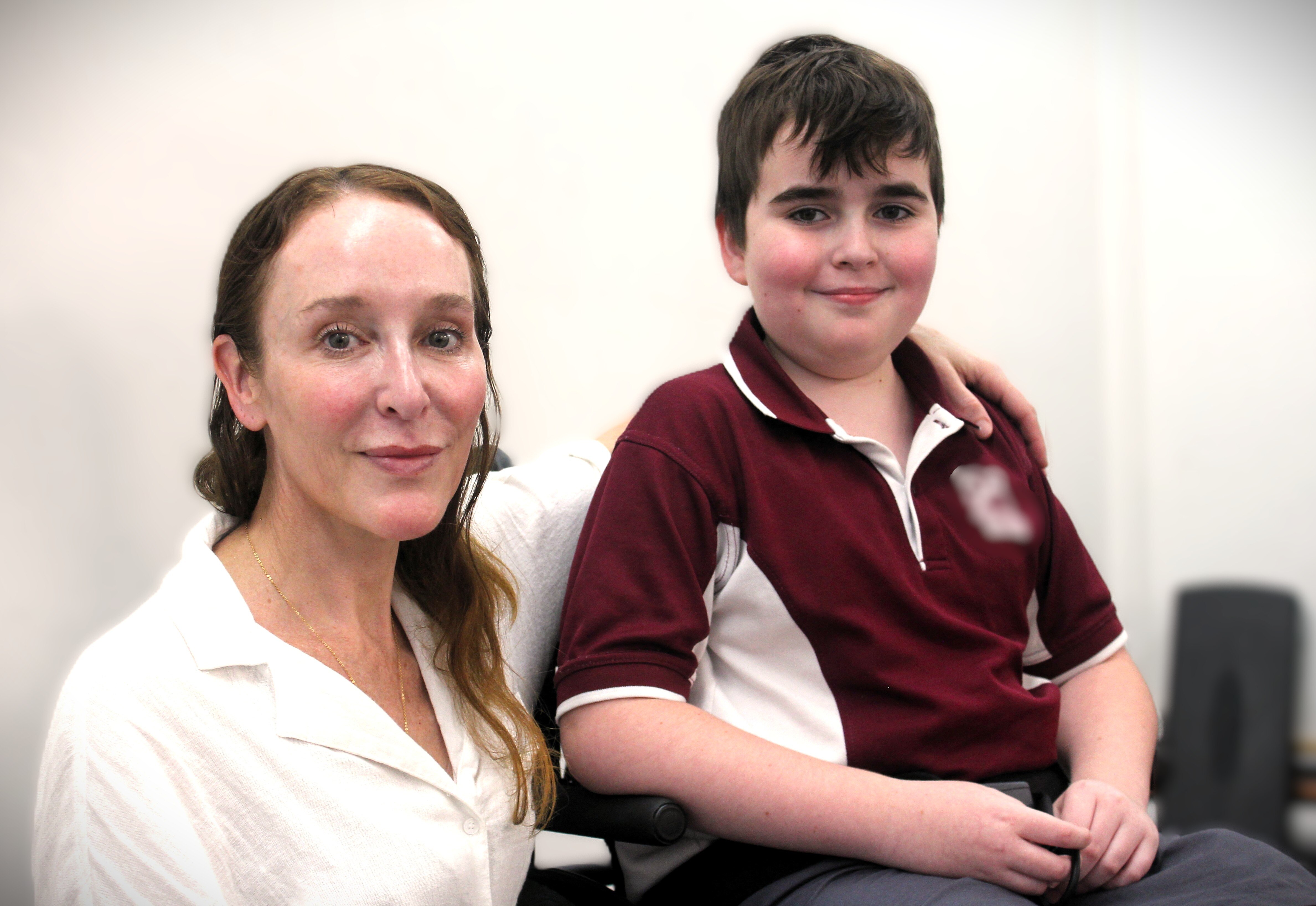 Uma mulher com longos cabelos escuros e uma camisa branca está sentada com o braço em volta de uma criança.