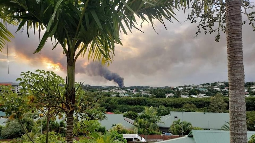 A tropical view over a leafy suburb with plumes of thick, black smoke over the buildings.