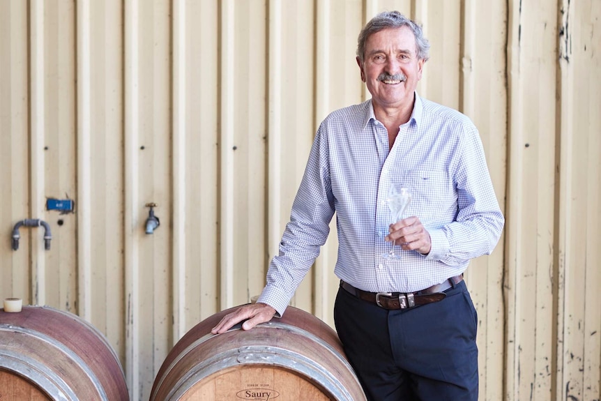 Man smiling as he leans on a barrel of wine.
