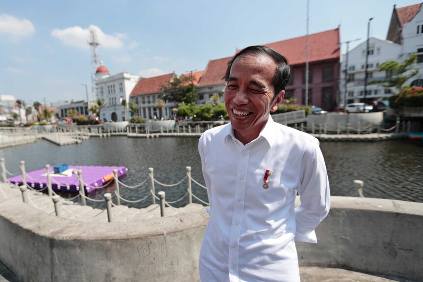 Indonesian President Joko Widodo smiles standing in front of a river in Jakarta.