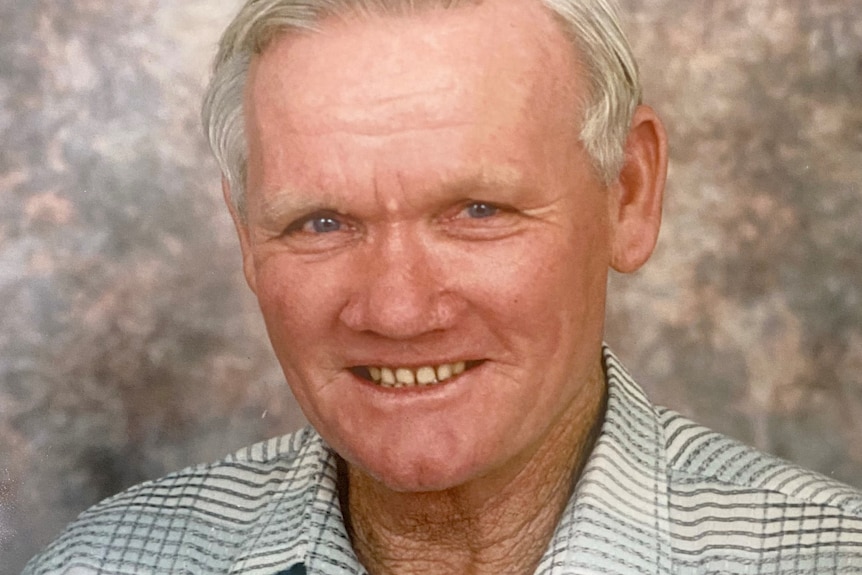 A headshot of a smiling older man, grey hair, white check shirt.
