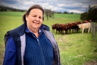 Woman stands in paddock with cattle in background.