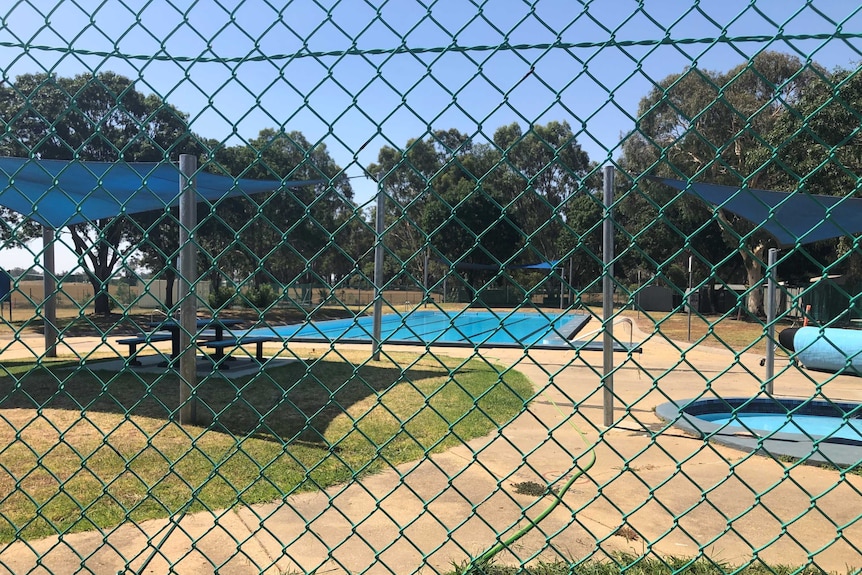 The empty pool is seen through cyclone fencing.