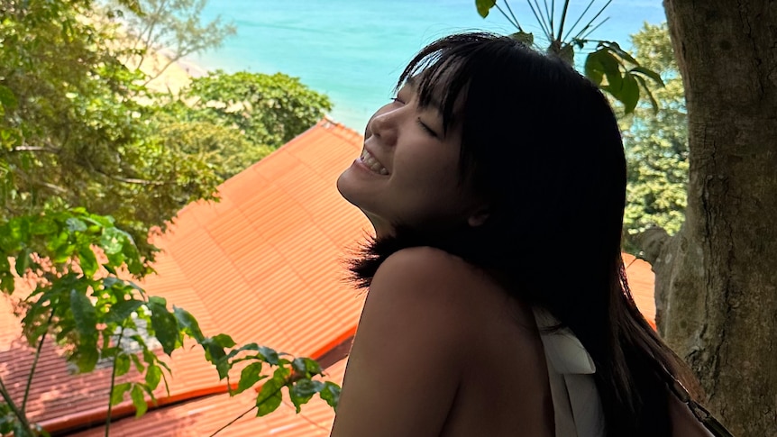 A woman stands under a tree and smiles