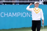 An Australian golfer grins and pumps her fist in celebration standing in front of a 'Champions' sign after winning a title.
