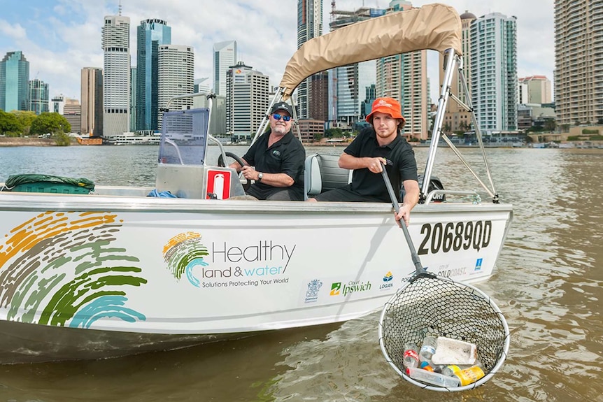 A man driving a boat with another man holding a fishing net filled with rubbish.