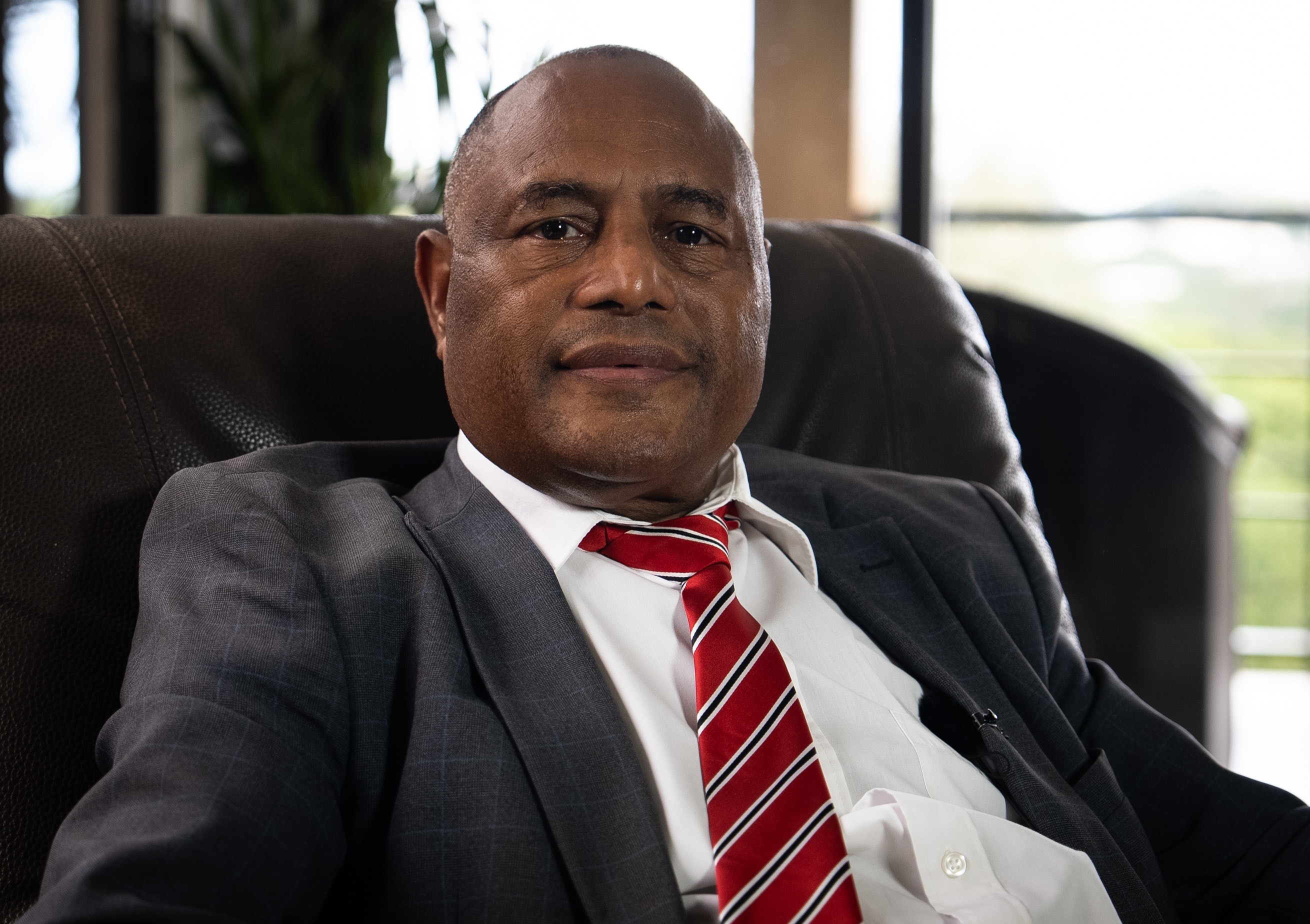 Un hombre con traje oscuro se recuesta en una silla de cuero en una oficina.