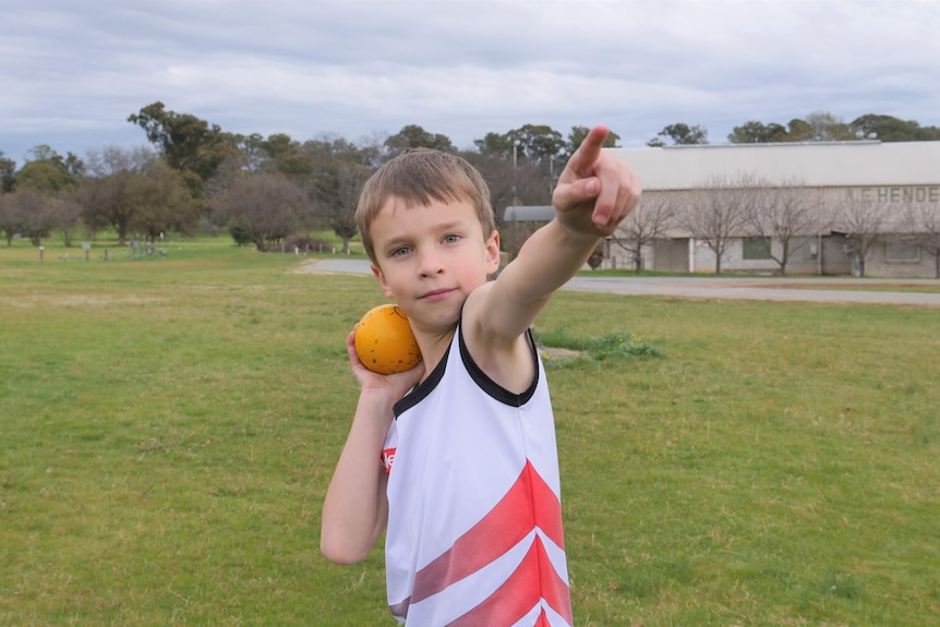 A kid gets ready to throw a shot put with his finger pointing out into the distance 