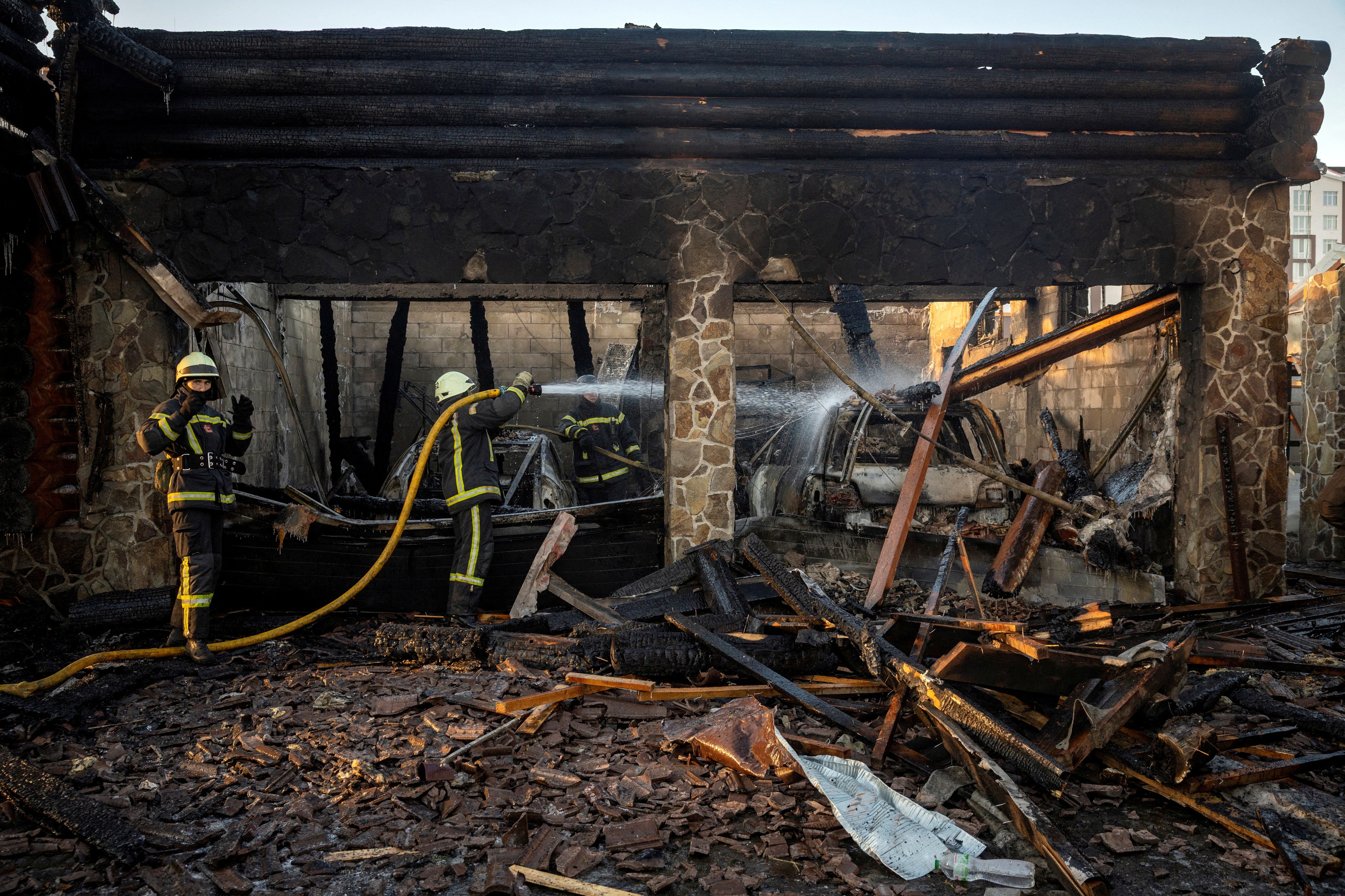 Two firefighters hose down a destroyed building after a drone strike