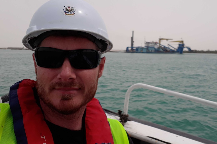 Michael John Mapley is seen in the left hand side of the frame wearing sunglasses and a hard hat, with the sea in the back.