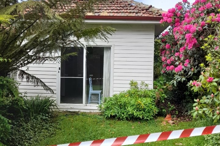 A photo of a white weatherboard home, with lush green garden surrounding it with tape around it