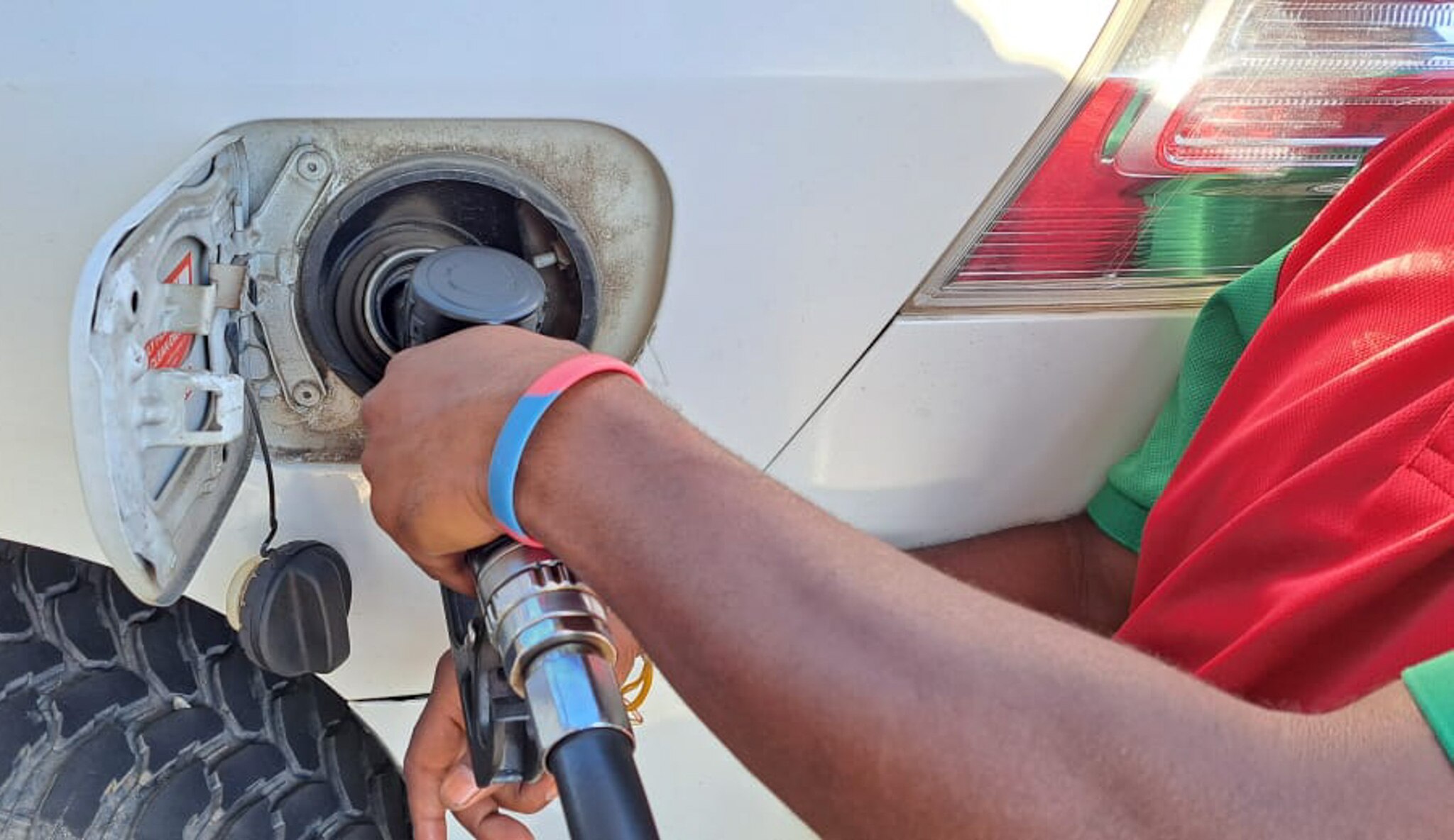 A person with their hand on a fuel pump puts fuel into their car.