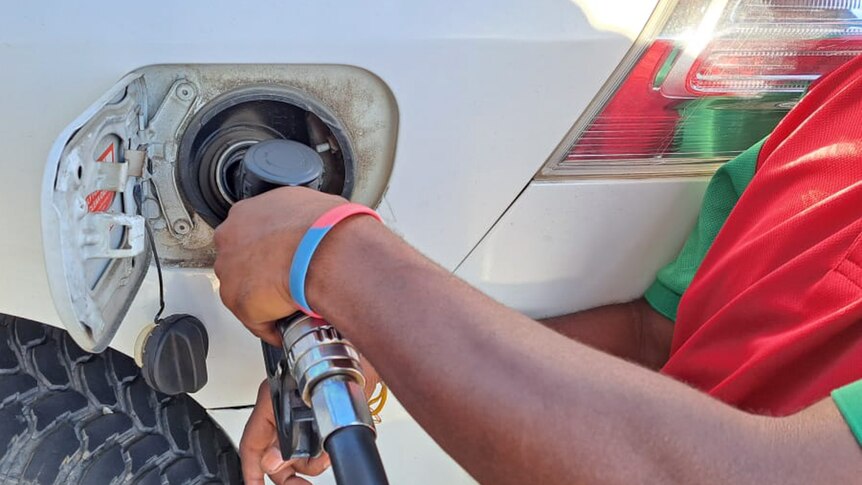 A person with their hand on a fuel pump puts fuel into their car.