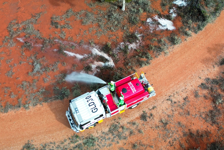 Firefighters spray their hoses into shrubs in the outback, as seen from above.