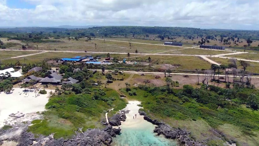 An aerial drone shot showing the empty paddock by the sea where Rainbow City will be built. Villas near the shore can be seen.