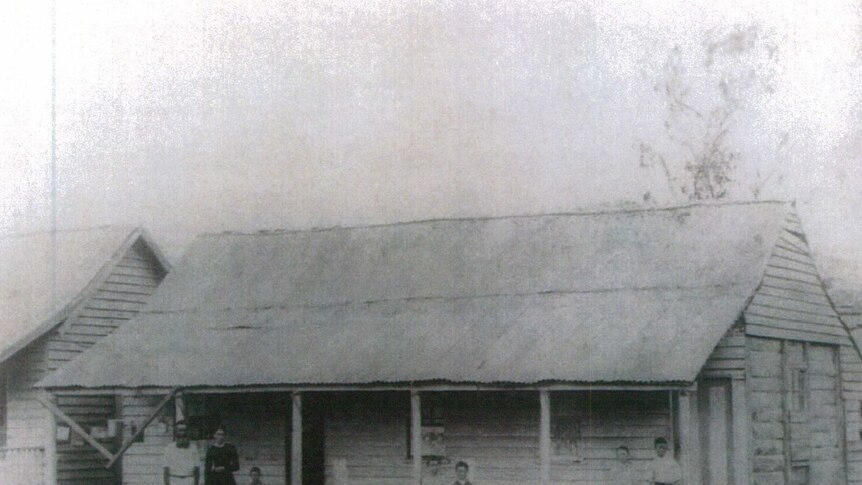 Two adults and five children stand in front of a homestead in a black and white photo