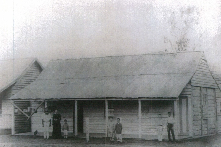 Two adults and five children stand in front of a homestead in a black and white photo