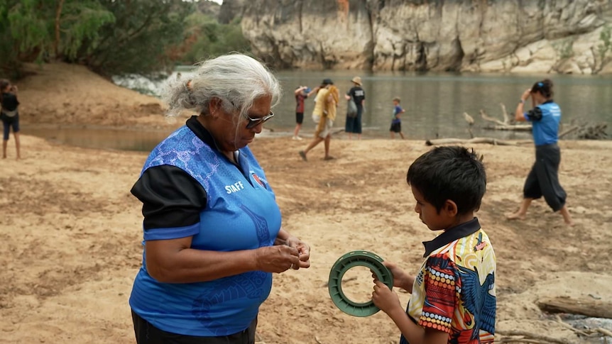 Indigenous woman stands with boy holding a fishing reel
