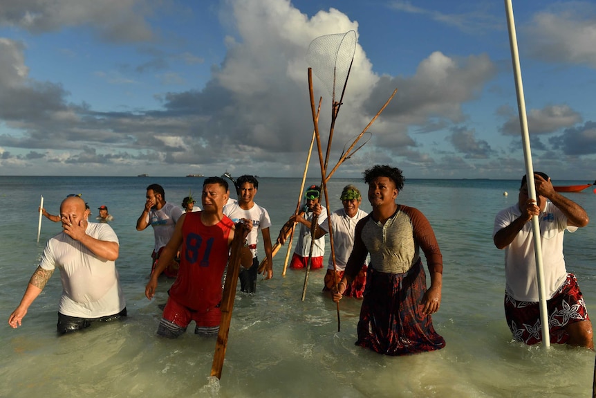 Fishermen walk out of the water with fishing equipment in Tuvalu's capital, Funafuti.