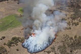 An aerial photograph of a spreading patch of fire in bushland, with masses of smoke rising from the fire.