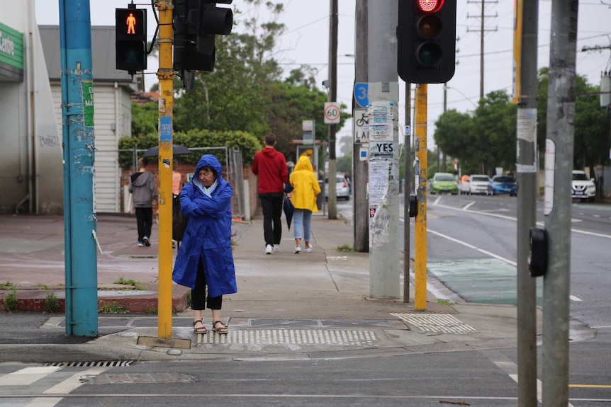 A woman wearing a blue raincoat crosses a street in gloomy weather.