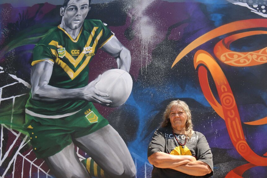 June Mills standing, arms folded in front of the new mural