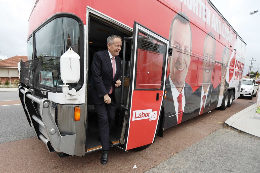 Bill Shorten smiles as he steps off a red bus with his face on it.