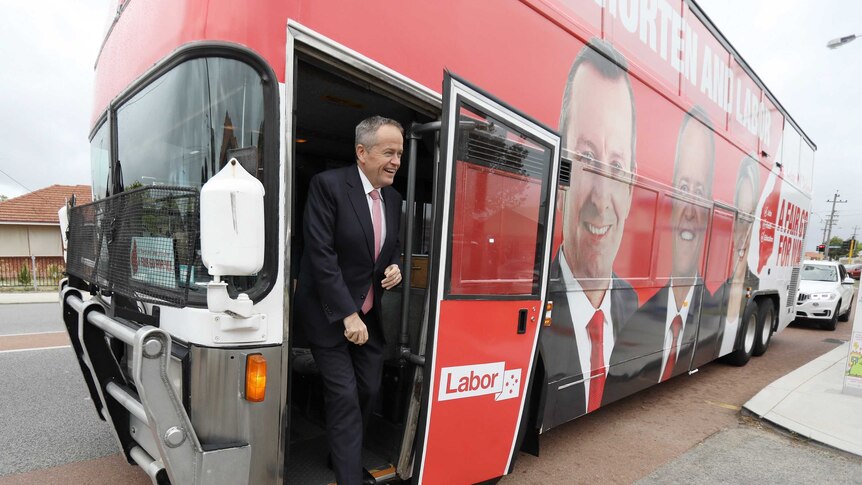 Bill Shorten smiles as he steps off a red bus with his face on it.