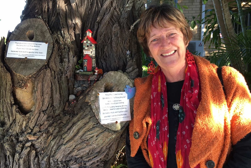 Woman stands beside tiny fire house in tree