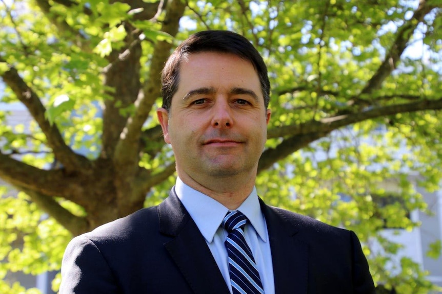 Headshot with a tree in the background.