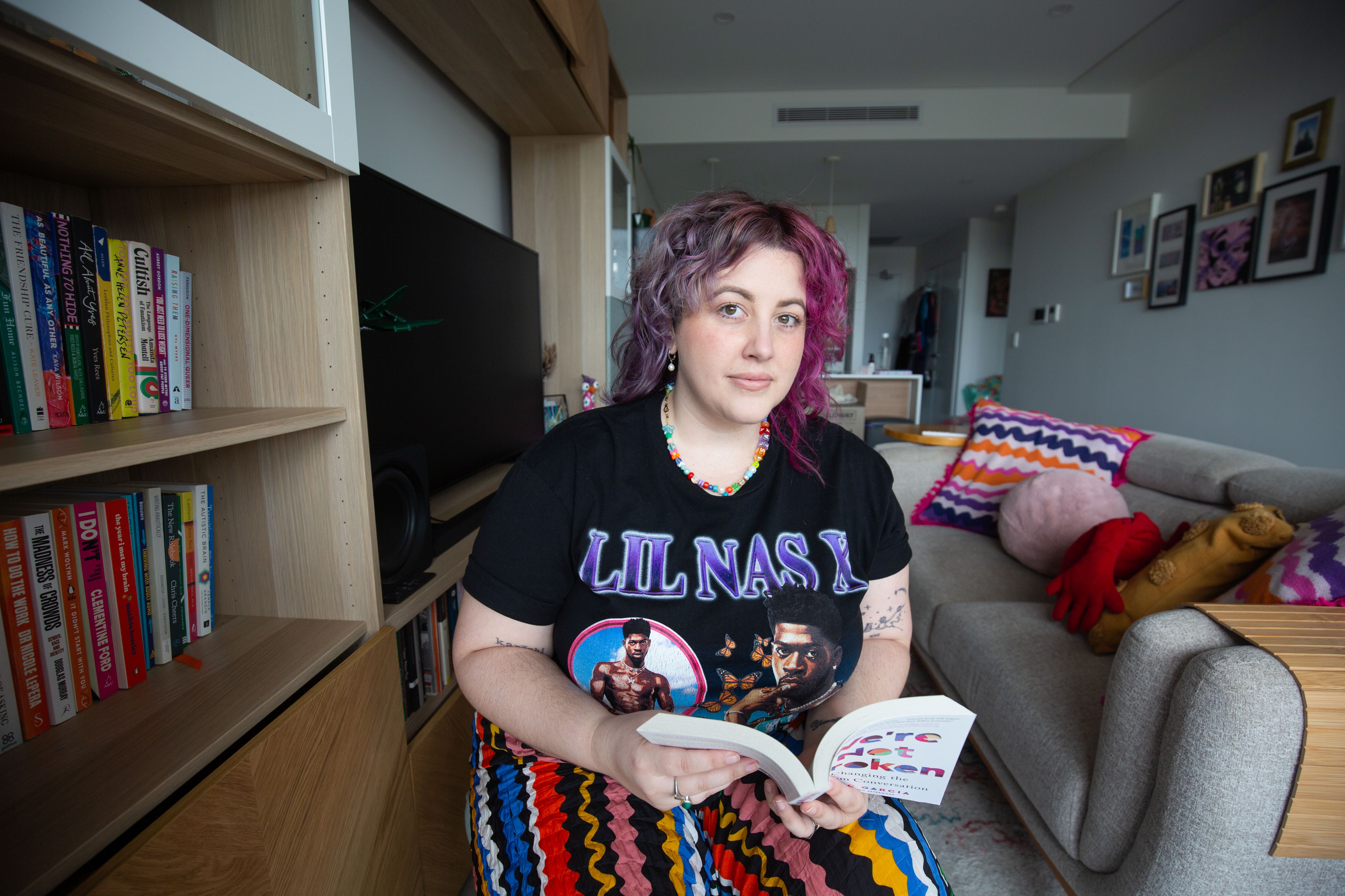A person with pink hair and a colourful skirt in their apartment on a cloudy day