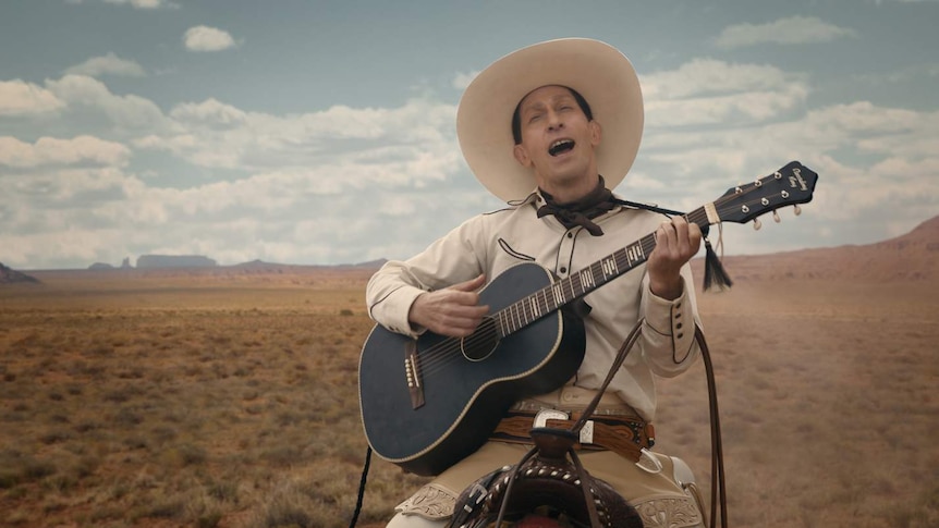 Man on horseback wearing light-coloured cowboy hat plays guitar and sings, Western plains behind him and blue sky above.