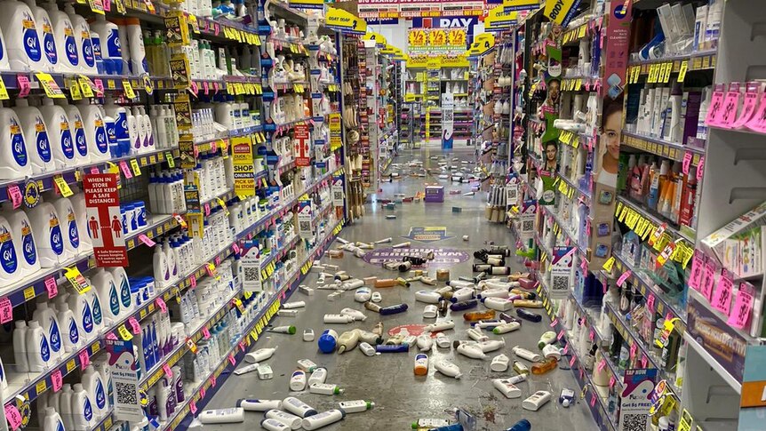 A grey chemist aisle in between shelves. Colourful products are strewn on the floor