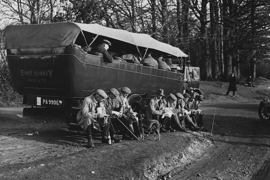 Men leaning against an old car with their dogs 