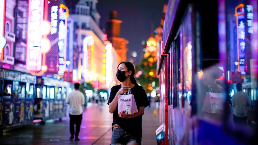 A young chinese woman in a face mask on a street bathed in fluorescent lights in Shanghai