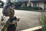 A picture of Pinocchio with a missing arm standing in front of some apartments.